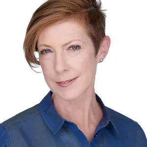 corporate headshot of woman with short cropped blonde pixie hairstyle and pearl stud earrings wearing navy blue button-down collared shirt photographed against seamless white studio backdrop with soft professional lighting by Lancaster Pennsylvania headshot photographer Richard Waine