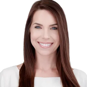 Professional business headshot of woman with long straight dark brown hair and bright smile wearing white sleeveless top photographed against seamless white studio backdrop with high-key professional lighting by Richard Waine Lancaster headshot photographer