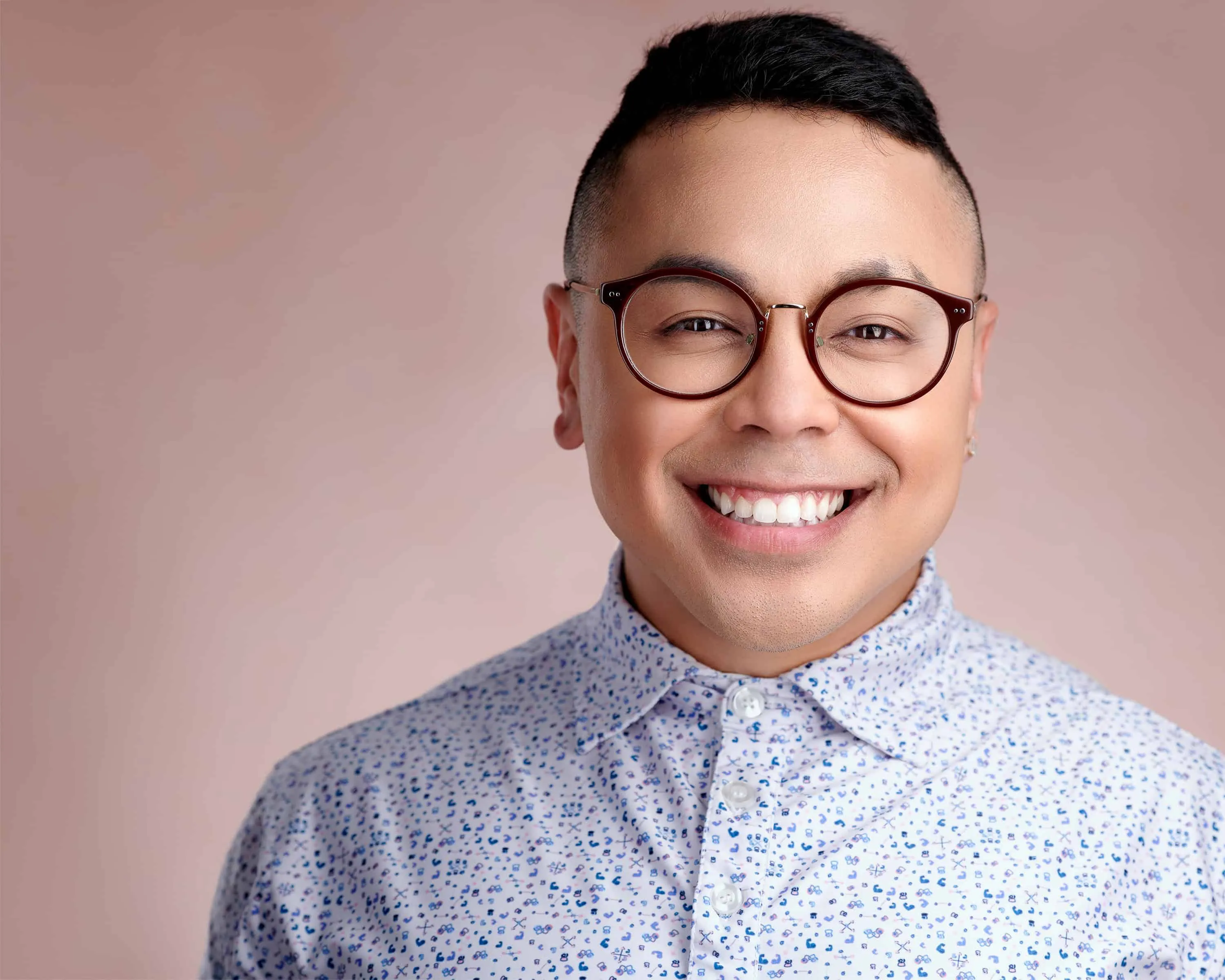 Cheerful subject with tortoise-shell glasses in white floral-patterned shirt on soft pink textured canvas background