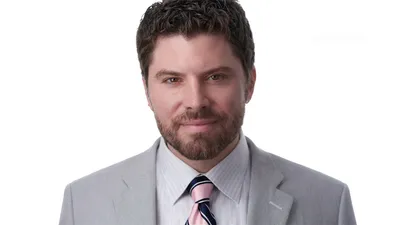 Pennsylvania plastic surgeon Dr. Bryan Cicuto professional medical headshot with short dark brown wavy hair, trimmed full beard, wearing light grey pinstriped suit jacket over white dress shirt with pink and navy diagonal striped tie, photographed on seamless white background by Lancaster Pennsylvania headshot photographer Richard Waine