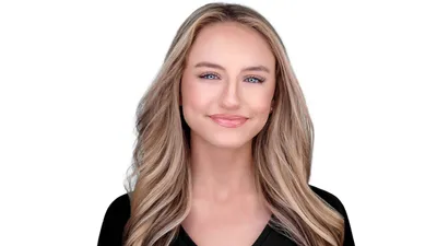 Woman with long flowing blonde waves and honey highlights, black v-neck top, warm confident smile, white studio background