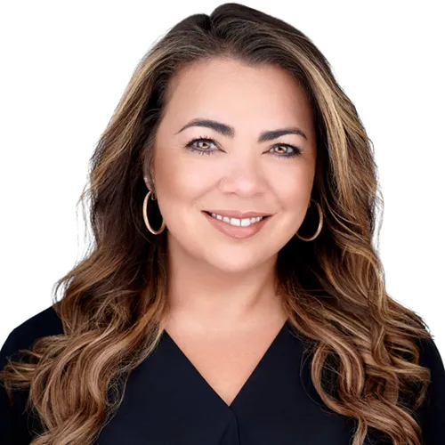 Professional business headshot of female marketing executive with long wavy dark brown hair with blonde balayage highlights and warm engaging smile wearing gold hoop earrings and black v-neck top photographed against white studio background by Richard Waine Photography