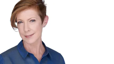 Female professional headshot with short auburn brown pixie cut hairstyle, silver pearl stud earrings, wearing navy blue collared shirt, photographed on seamless white background by Lancaster Pennsylvania headshot photographer Richard Waine, business portrait example