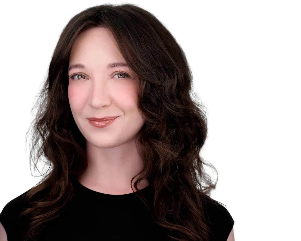 Professional headshot of woman with long wavy dark brown hair in black top, smiling against white studio background, headshot made by Richard Waine in Lancaster Pennsylvania