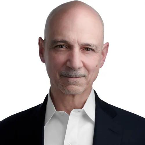 Professional LinkedIn headshot of man with clean-shaven head and trimmed gray goatee and mustache wearing navy blue suit jacket with white open-collar dress shirt photographed against seamless white backdrop with professional lighting by Richard Waine Photography