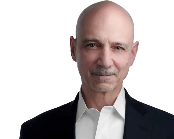 Professional LinkedIn headshot of man with clean-shaven head and trimmed gray goatee and mustache wearing navy blue suit jacket with white open-collar dress shirt photographed against seamless white studio backdrop with soft directional lighting by Richard Waine Photography LinkedIn headshot photographer serving Lancaster York Harrisburg Pennsylvania Baltimore Maryland