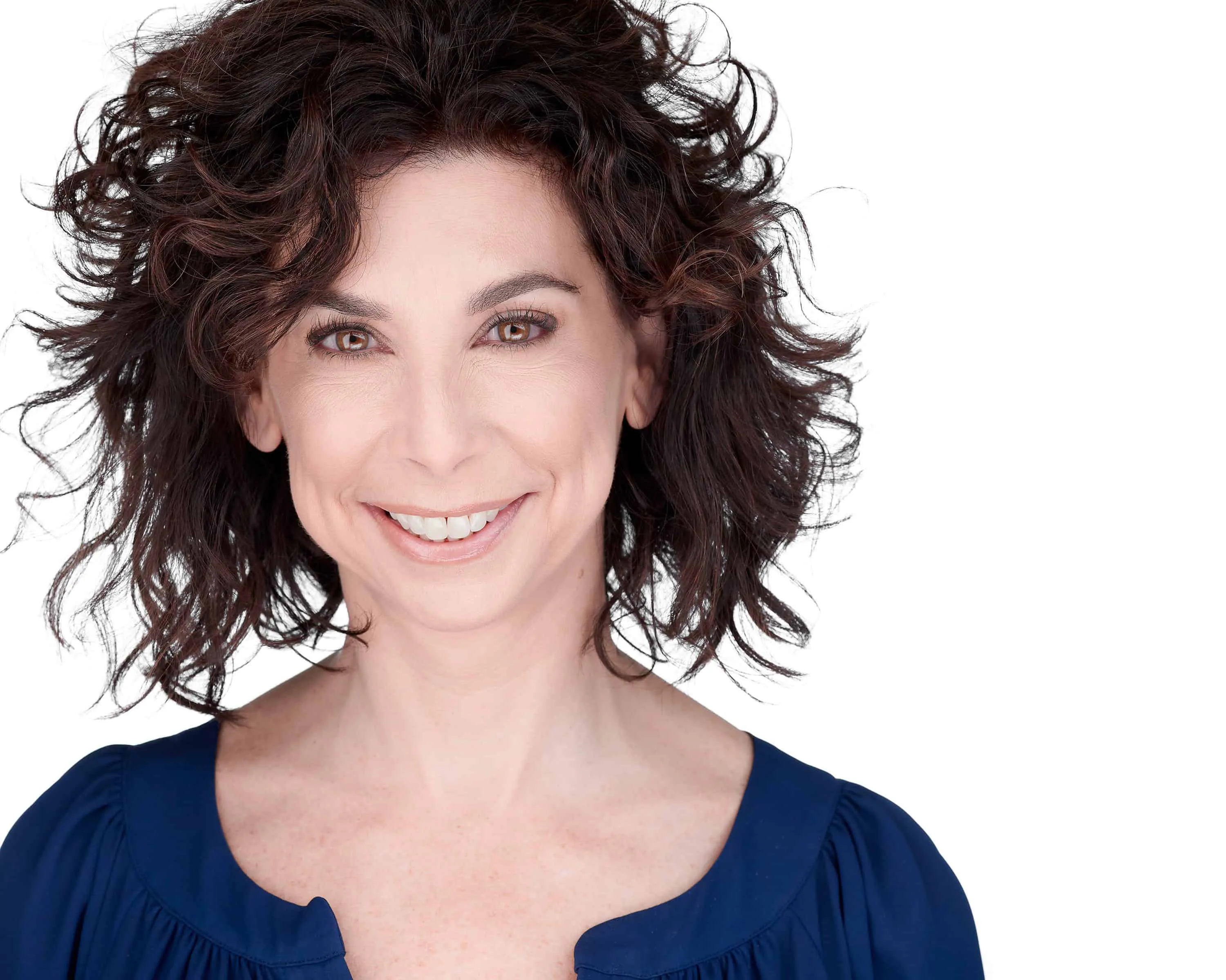Professional headshot of J. Hilburn stylist Lisa Torba with voluminous dark brown curly shoulder-length hair and warm smile wearing navy blue scoop neck top photographed against seamless white studio backdrop with professional studio lighting by Richard Waine Photography Lancaster Pennsylvania