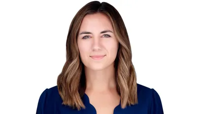 Professional headshot of young Caucasian woman with shoulder-length wavy brown hair with blonde highlights and side part wearing navy blue top showing confident approachable expression with natural subtle closed-mouth smile photographed against seamless white background with professional high-key lighting by Richard Waine Photography Lancaster Pennsylvania