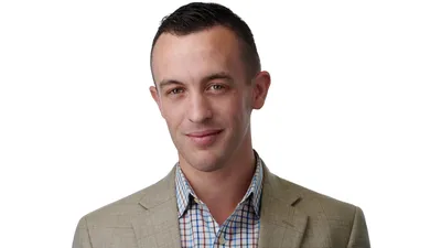 Male professional headshot with short dark brown hair, wearing tan beige sport coat over blue white and orange plaid button-down shirt, photographed on seamless white background by Lancaster Pennsylvania photographer Richard Waine