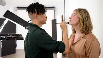 Behind the scenes image of makeup artist Lionel Adriano of Revolve Atelier applying makeup with a brush to set designer Liz Riden at Richard Waine Photography studio in Lancaster Pennsylvania