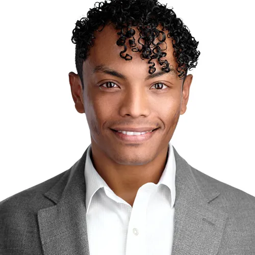 Professional business headshot of Argentinian male marketing executive with short curly black hair styled with defined curls and warm bright smile wearing charcoal gray textured suit jacket over crisp white dress shirt photographed against white studio background by Richard Waine