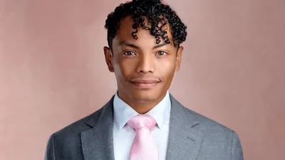 Professional in charcoal suit with pink silk tie and curly hair against dusty rose hand-painted canvas backdrop
