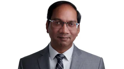 Male professional headshot with short black hair, rectangular frame eyeglasses, wearing grey suit jacket over white dress shirt with grey black and white checkered tie, photographed on seamless white background by Lancaster Pennsylvania headshot photographer Richard Waine