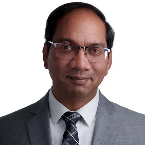 Professional executive headshot of man with short dark hair wearing rectangular frame eyeglasses charcoal gray suit jacket over white dress shirt with black and gray plaid patterned tie photographed against white background by Richard Waine Photography.