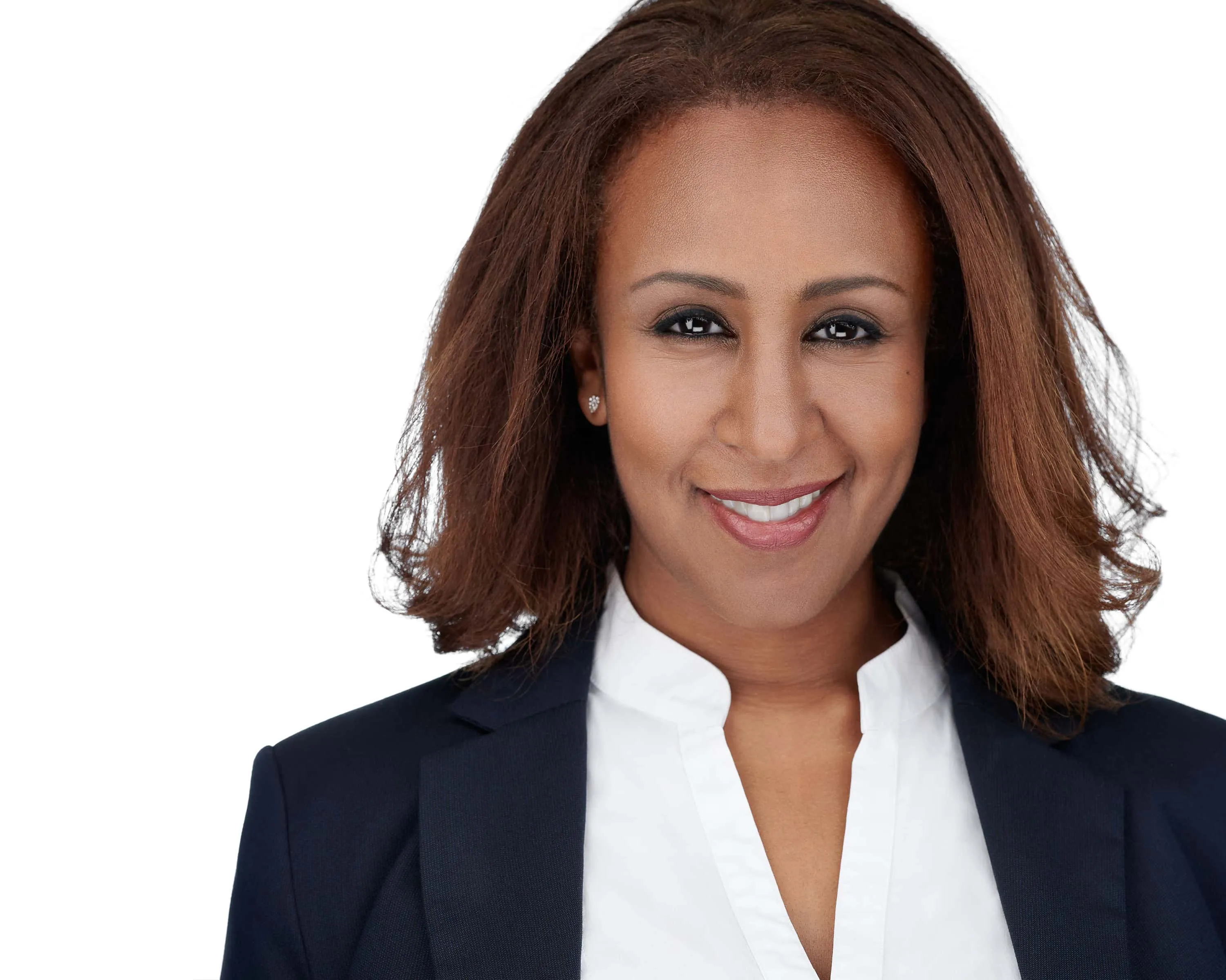 Professional business headshot of African-American woman with shoulder-length reddish-brown wavy hair and warm smile wearing navy blue blazer layered over white collared blouse with diamond stud earrings photographed against seamless white backdrop by Richard Waine