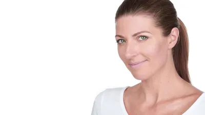Woman with brown hair in sleek ponytail wearing white top against white studio background with warm smile